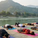 Group practicing 200 hour yoga teacher training in Rishikesh, by the sacred Ganga River in serene morning light.
